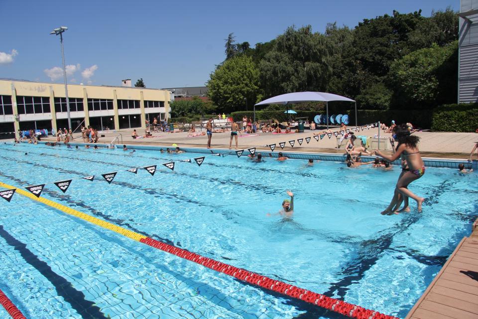 Vue sur le bassin extérieur du stade nautique. Deux enfants sautent du ponton dans la piscine. 