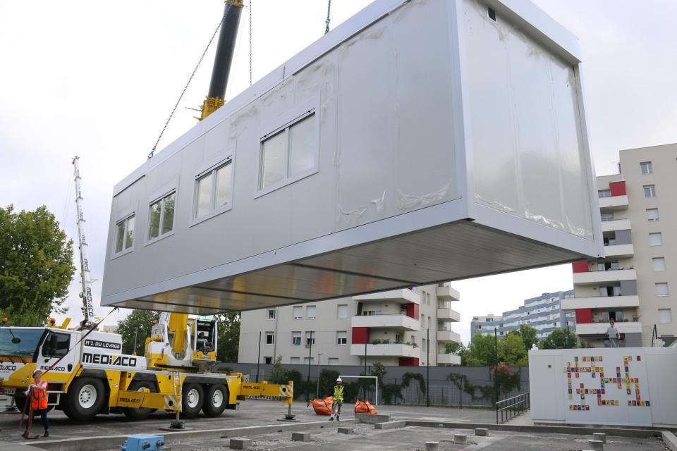 Un module est soulevé, déplacé et positionné dans la cours  de l'école par une grue.