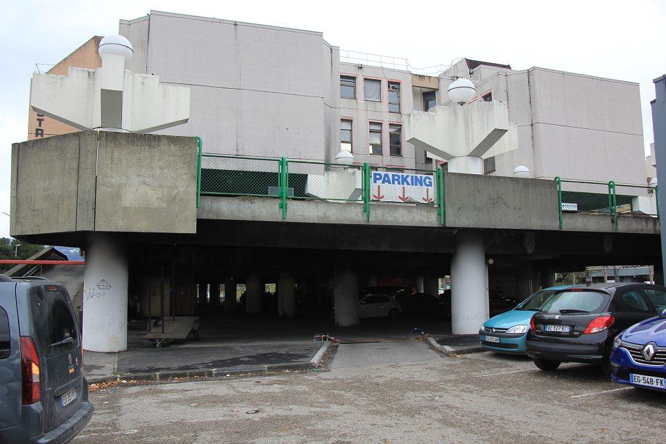 Vue du parking du Stratège. Plusieurs voitures sont garées. Il s'agit d'un parking extérieur avec un étage.