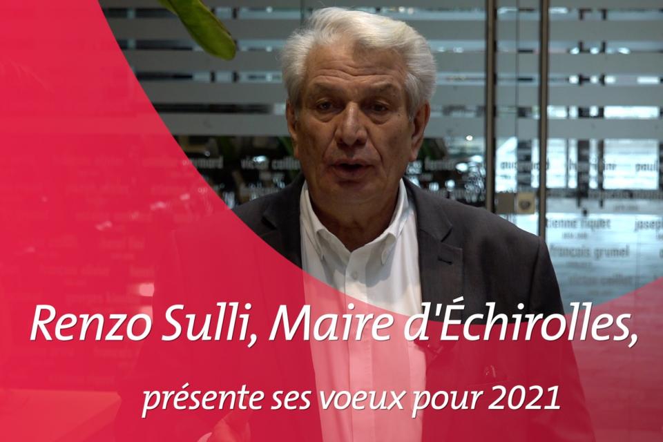 Le Maire d'Echirolles se tient en costume noir et chemise blanche, devant la salle des mariages. Il présente ses voeux aux échirollois-es pour l'année 2021. Sur cette image, une contre forme arrondie rose (charte graphique des vidéos de la ville) introduit la vidéo.