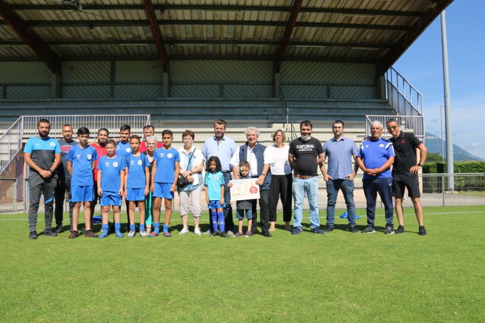 Photo prise à l'occasion de la remise des premiers Chèques sport avec les élus de la Ville, OSE et le FCE. Nous voyons le maire et les élu-es qui posent sur le terrain de foot avec les jeunes joueurs et les encadrants du club de foot.