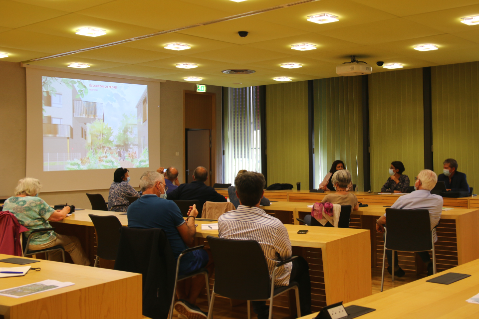 Photo d'une réunion de concertation autour du projet d'aménagement du secteur République qui s'est tenu à l'hôtel de ville. En salle du conseil, les habitant-es et les élu-es sont face à face, un diaporama est projeté sur le mur. 